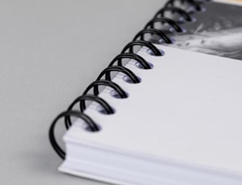 Gros plan sur la finition d'un document imprimé montrant une reliure à spirale métallique noire (Wire-O).