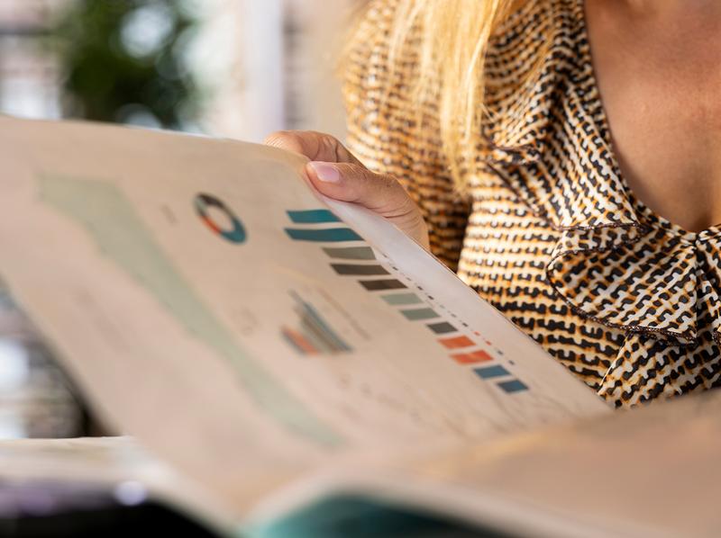 Gros plan d'une personne consultant un rapport d'entreprise imprimé, ouvert sur une page présentant des graphiques statistiques en couleurs.